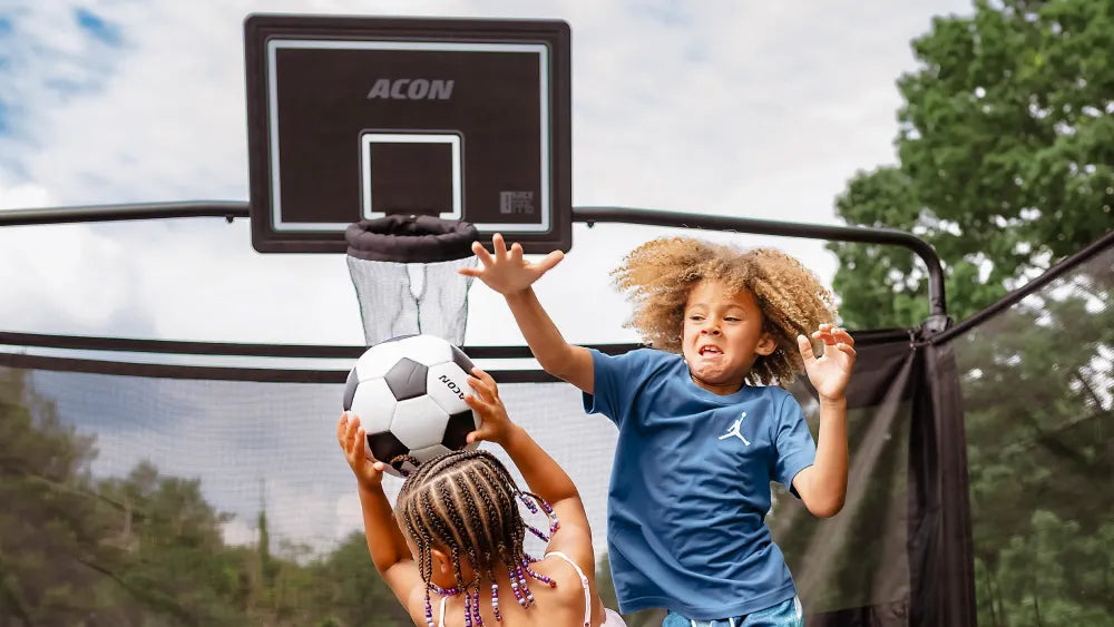 Kinder spielen mit dem ACON Basketball Hoop auf einem Acon X Trampolin.
