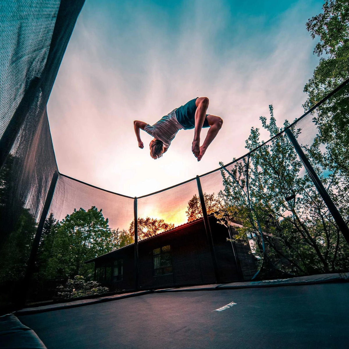 Mann macht einen Rückwärtssalto auf einem Trampolin im Sonnenuntergang 