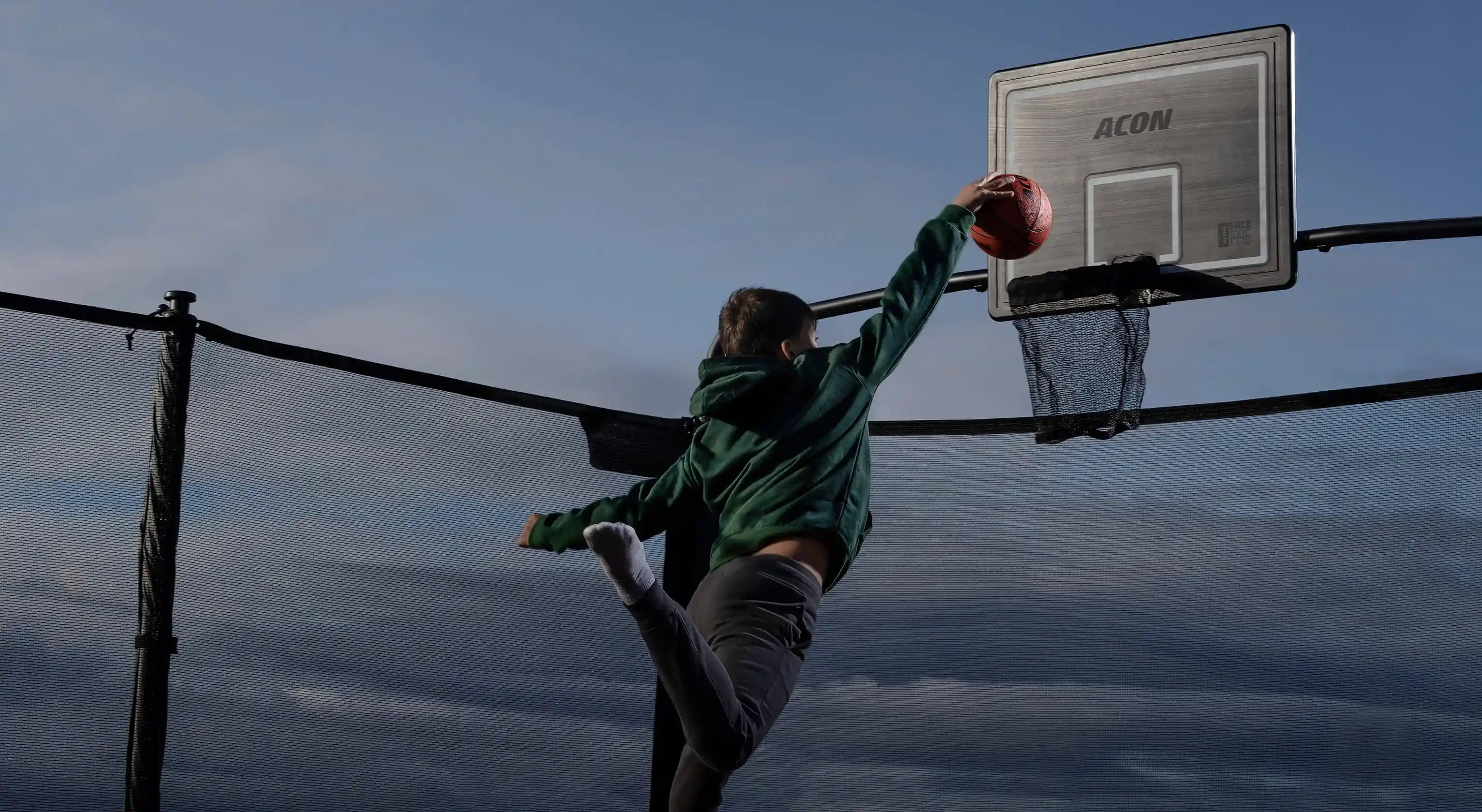 Ein Junge wirft einen Basketball in den Basketballkorb des Trampolins.