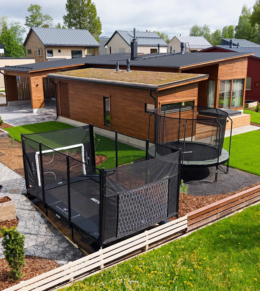 Zwei Acon Trampoline im Hinterhof eines modernen Hauses. Eines davon ist ein teilweise eingesetztes Trampolin.