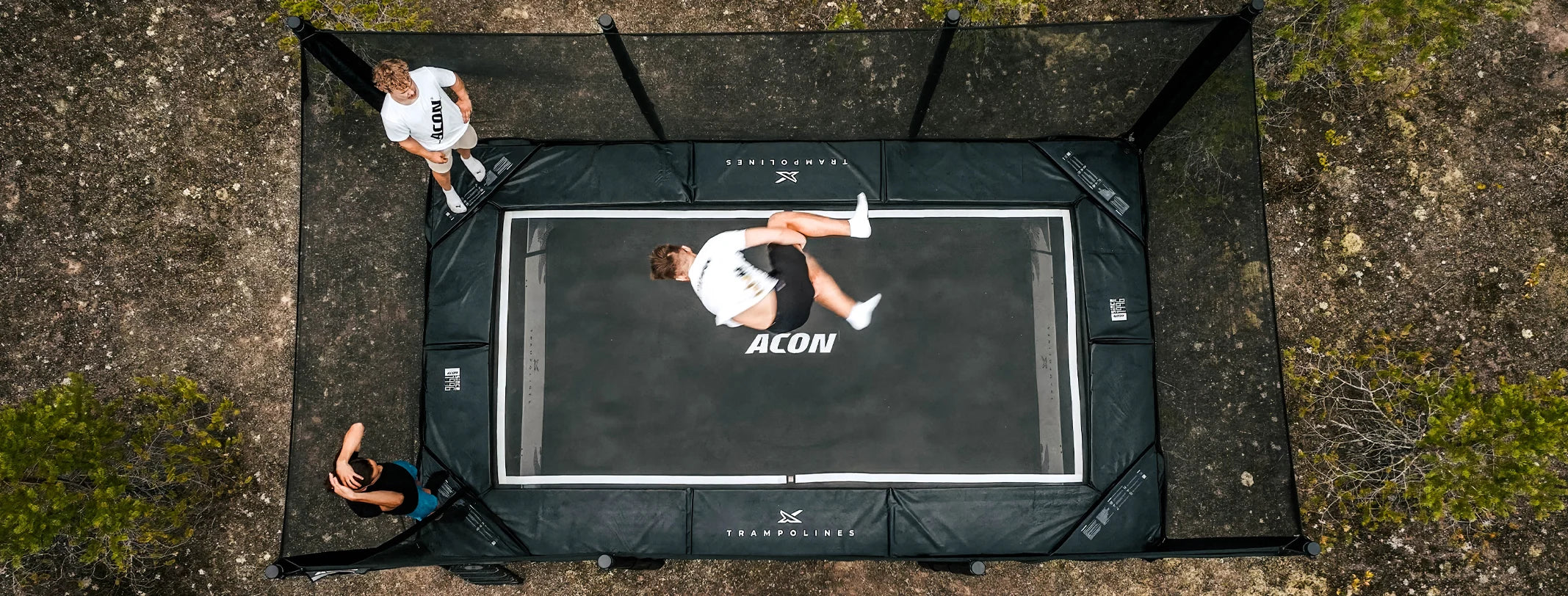 Drei Personen führen Tricks auf einem Acon X 17ft-Trampolin im Freien aus.
