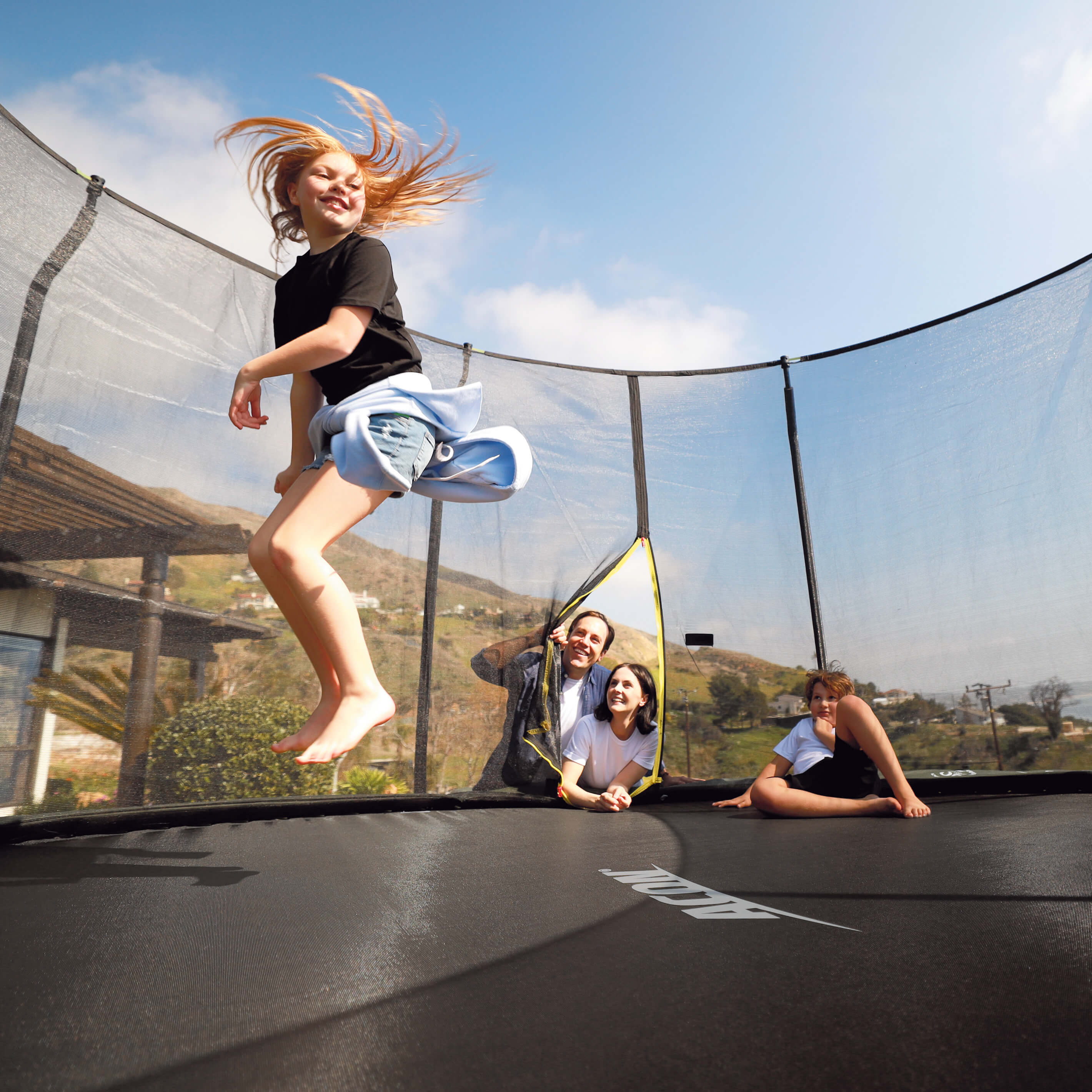 Mädchen springt auf einem Acon-Trampolin, Familie schaut zu.