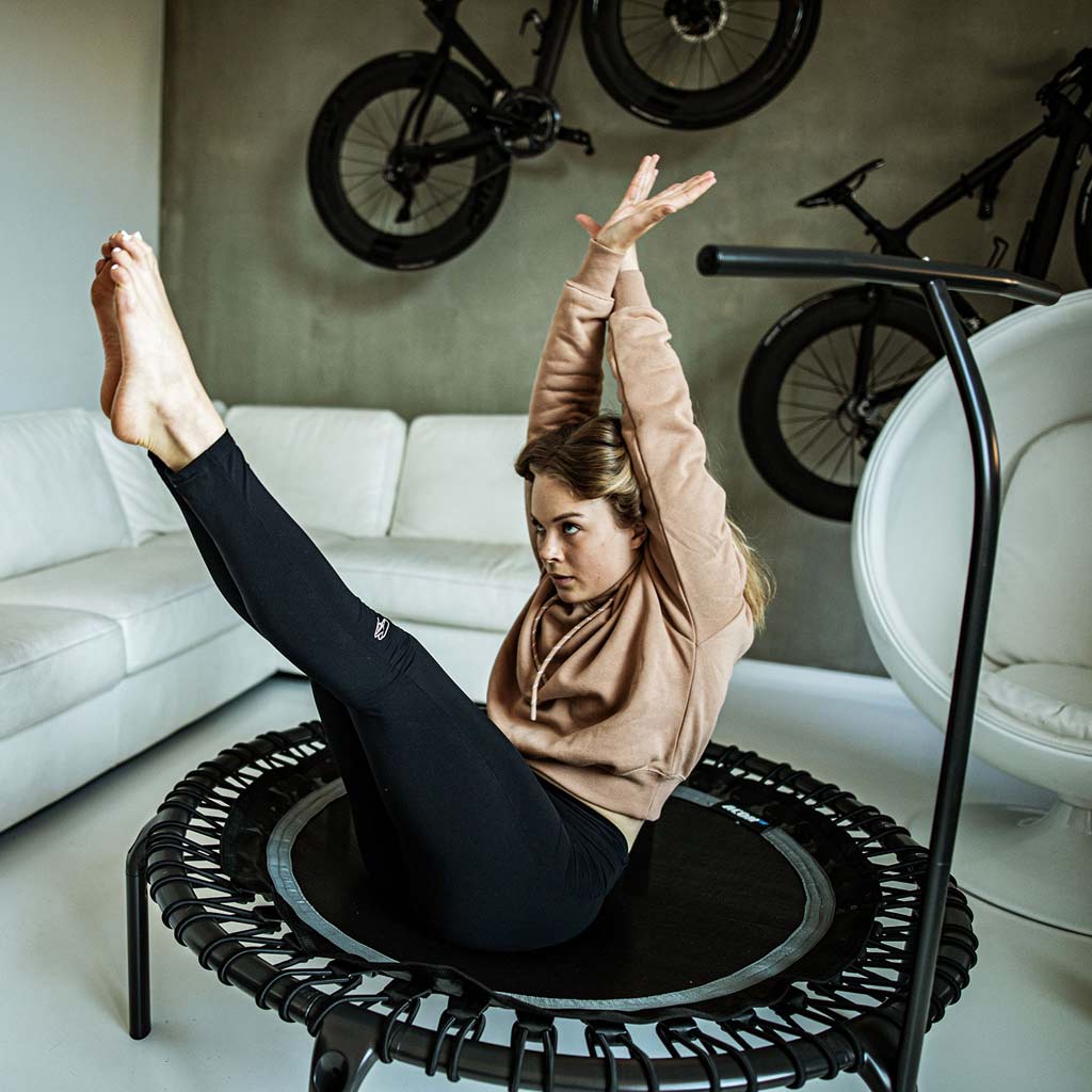 Frau trainiert im Wohnzimmer auf einem schwarzen runden ACON FIT 1,12m-Trampolin.