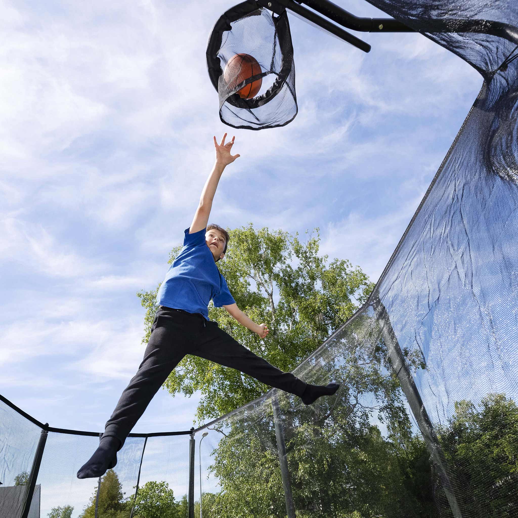 Ein Junge wirft einen Basketball in den Basketballkorb des Trampolins.