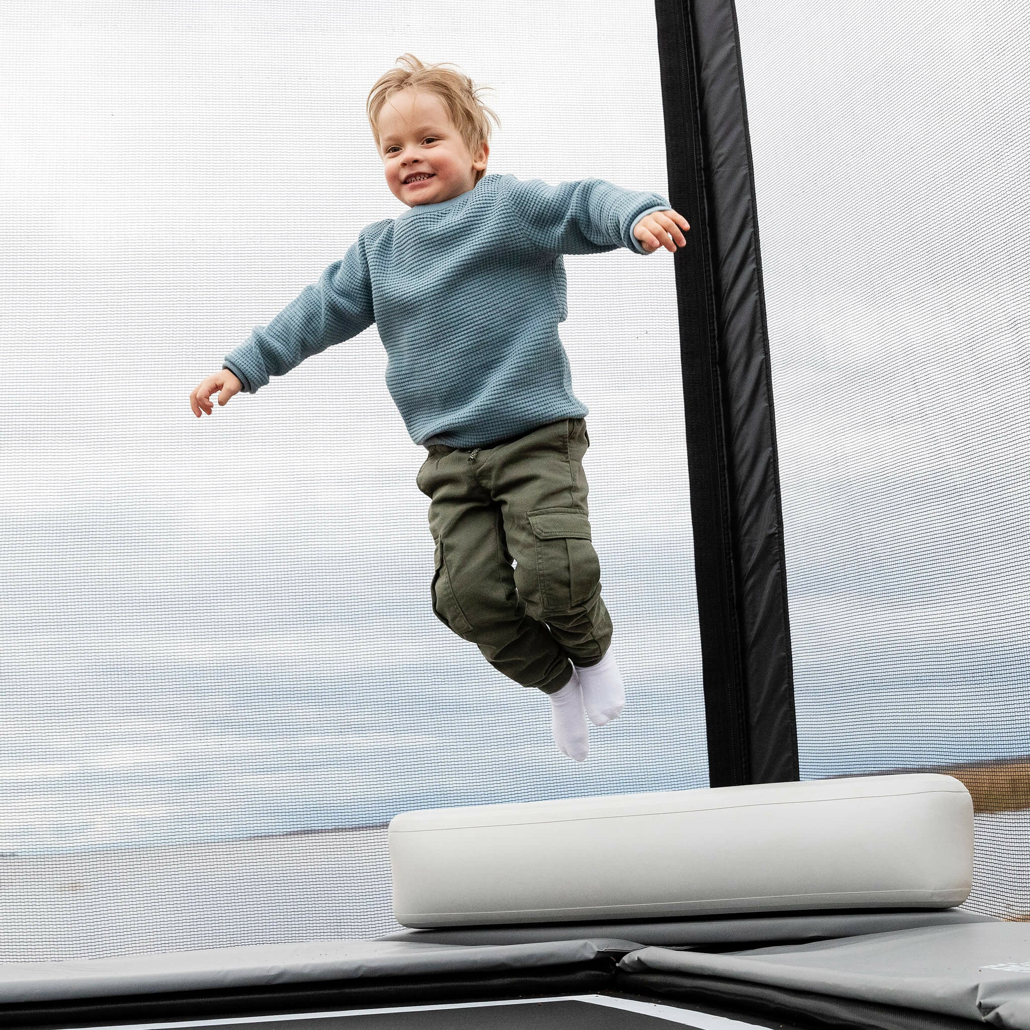 Ein kleiner Junge springt von der Spitze des Acon X Inflatable Triangle Blocks auf ein Trampolin.